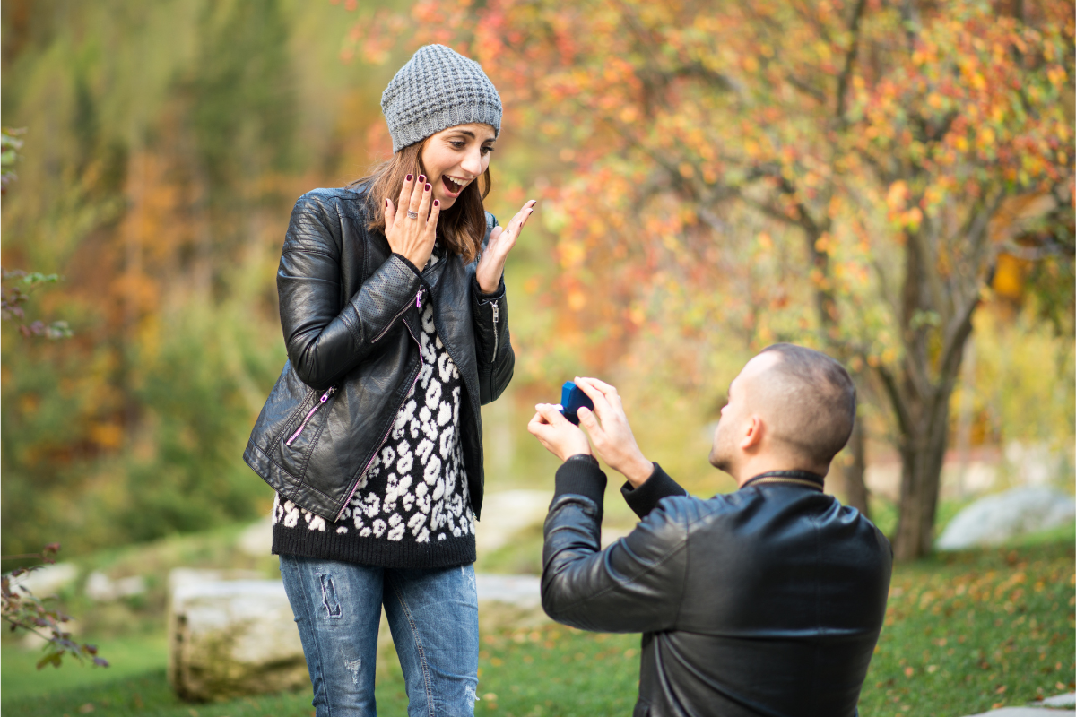 A man proposing to his girlfriend on a beautiful sunny day with a ring in hand.