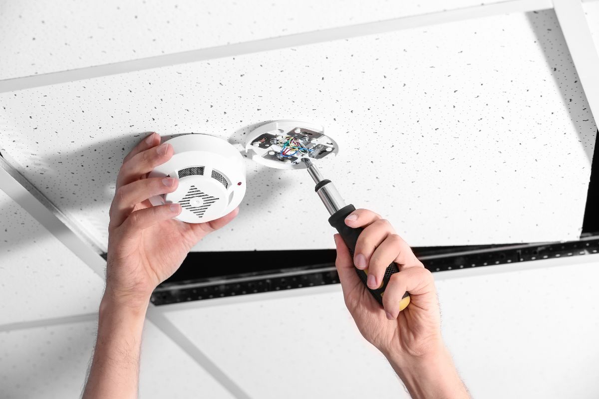 Person cleaning a smoke alarm to ensure proper functionality and home safety