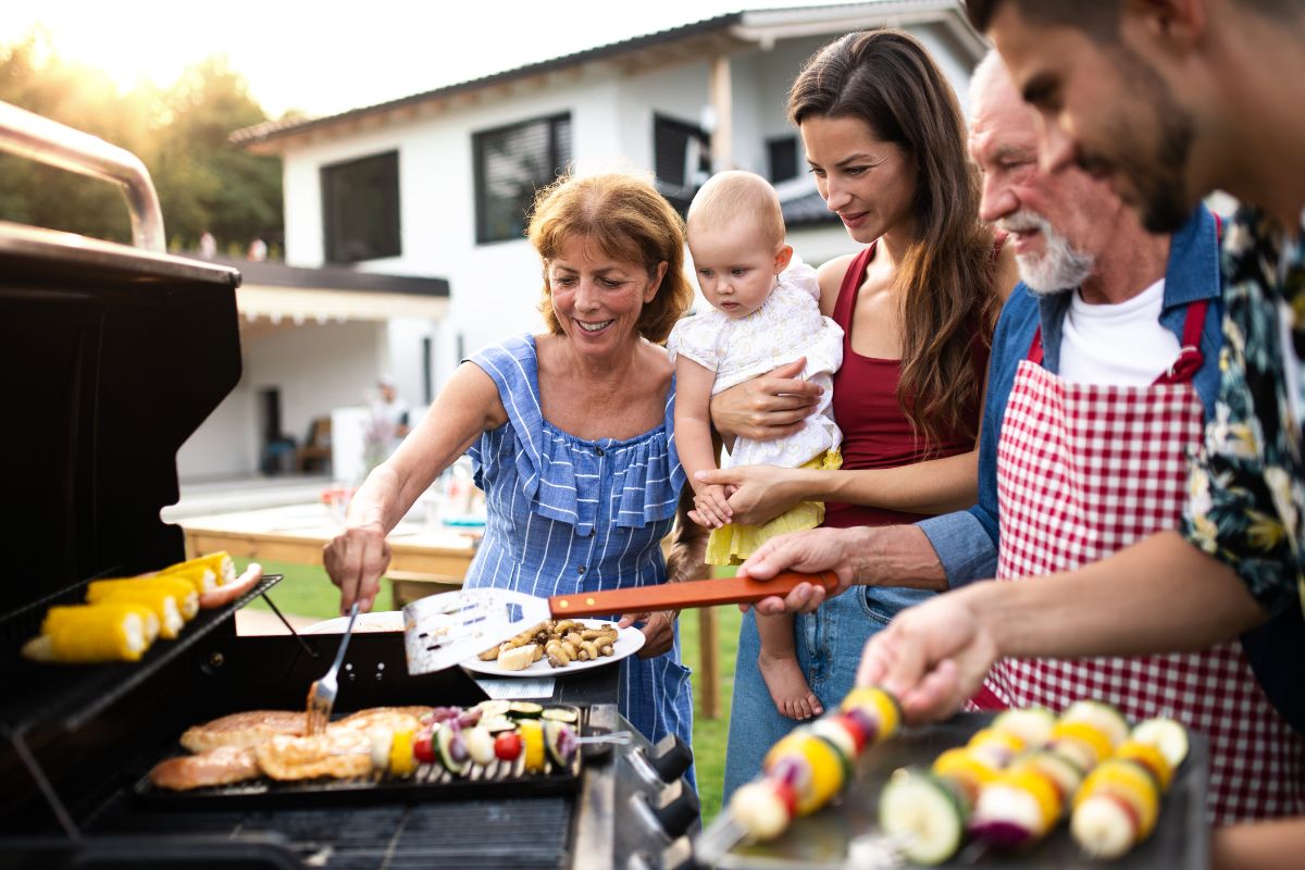 A smiling family gathered around a grill in the backyard, sharing food and enjoying a sunny afternoon together during a backyard BBQ.