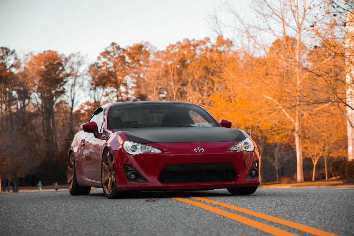 Driver inspecting car tires and fluids on a crisp fall day to stay safe and confident during autumn travels.