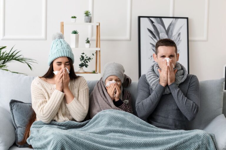 Person wrapped in a cozy scarf outdoors, sneezing while autumn leaves fall around them, illustrating the challenge of distinguishing seasonal allergies from a common cold.