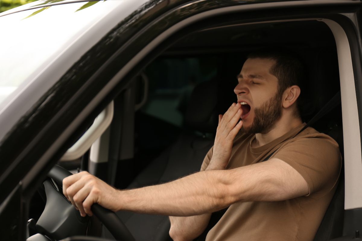 Tired man yawning while sitting in his car, showing signs of drowsy driving