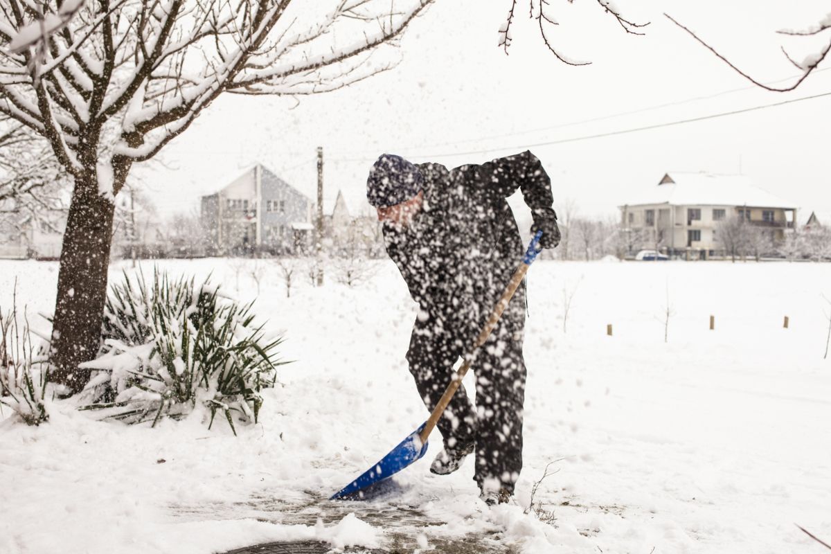 Person shoveling snow safely on a driveway during winter.