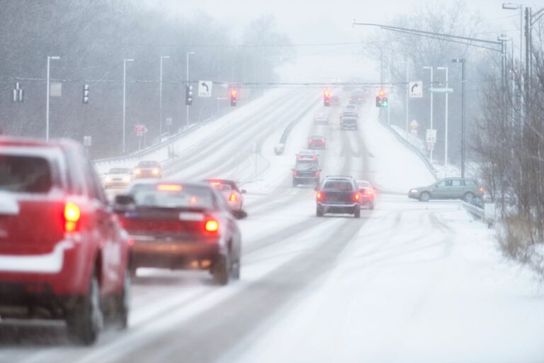 Car driving cautiously on wet icy road with headlights on, symbolizing safe driving practices in extreme weather conditions