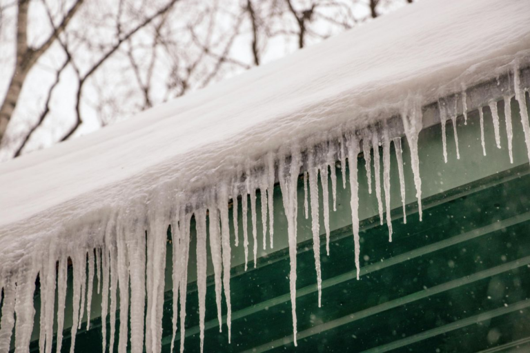 Thick ice dams forming along the edge of a snow-covered residential roof during winter