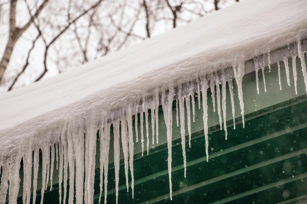 Thick ice dams forming along the edge of a snow-covered residential roof during winter
