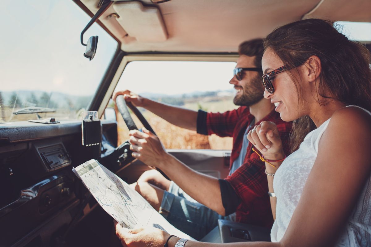 Young couple checking a map beside their packed car before starting a road trip adventure.