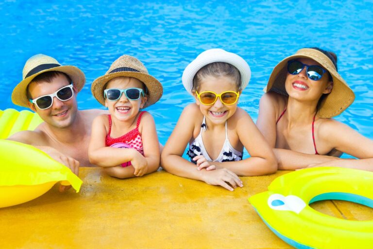 Family swimming in a pool while parents guide young children learning to swim safely and confidently