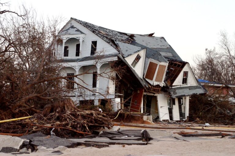 A severely damaged home with a collapsed roof, broken windows, and scattered debris after a powerful hurricane passed through the area.